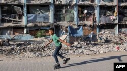 一个男孩滑着旱冰鞋路过加沙地带北部贾巴利亚一个收容所内的一栋被毁建筑物旁。(2024年9月8日)
