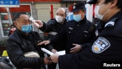 湖北武汉街头设立的检查卡社区工作人员检测行人的体温,警察检查其身份文件。(2020年2月20日)