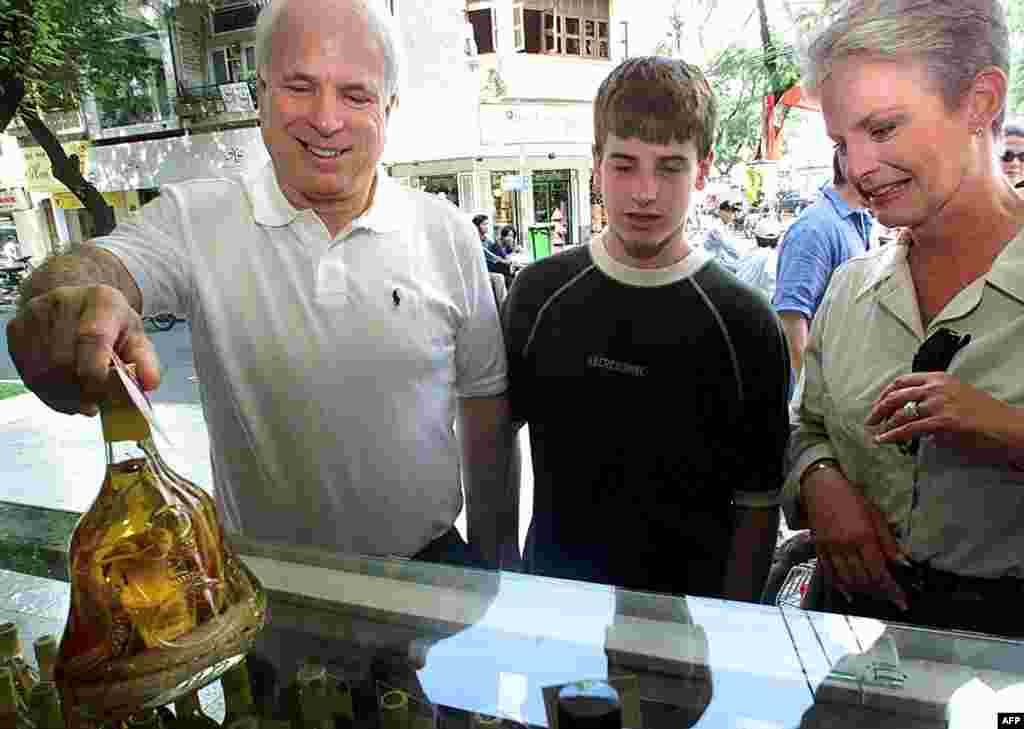 Ông McCain cùng con trai Jack và vợ Cindy ngắm nghía một chai rượu rắn trong một chuyến đi mua sắm ở Thành phố Hồ Chí Minh, ngày 28 tháng 4 năm 2000. Ông và gia đình đến đây nhân kỉ niệm 25 năm ngày kết thúc Chiến tranh Việt Nam.    