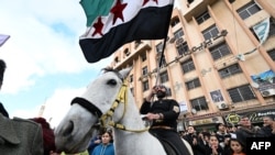 一名骑马男子挥舞着独立时代的叙利亚国旗,人们庆祝阿萨德政权的垮台。(法新社:2024年12月13日)