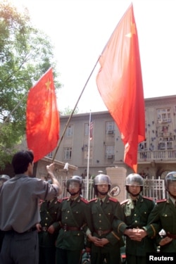 1999年5月10日,中国示威者在美国驻华使馆外面挥舞国旗。中国武警列队保护使馆。使馆墙壁被抗议美国轰炸中国驻南斯拉夫使馆的人用砖石砸得伤痕累累