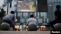 北京居民坐在一家商场外观看电视节目。(2016年7月16日)