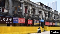 一名戴着口罩的骑车男子在武汉街头被封堵的商店旁驶过。(2020年3月5日)