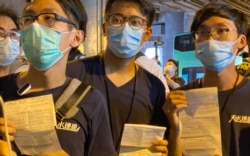 3名元朗区议员伍健伟(左起)、陈树晖、林进,7月19日下午在元朗西铁站举行7-21袭击事件一周年记者会,未开始已经被大批防暴警察包围截查,他们向记者展示警方发出的违反限聚令告票,罚款2千港币,折合约260美元 (美国之音/汤惠芸)