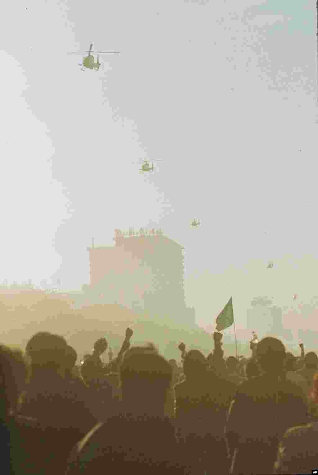 中国的军用直升机掠过天安门广场上空,北京大学的学生们此时挥舞着拳头和旗帜(1989年5月21日)