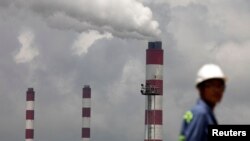 资料照:浙江宁波港的一名工人站在火力发电厂的烟囱前。