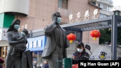 资料照片:中国武汉市,一名女子正走过带着口罩的雕塑面前。期间,世卫组织新冠溯源专家小组正在武汉考察。(2021年1月29日)