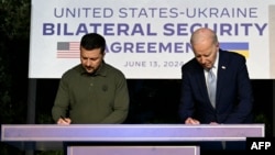 အမေရိကန်သမ္မတ Joe Biden (ယာ) နဲ့ ယူကရိန်းသမ္မတ Volodymyr Zelensky (ဝဲ) တို့ G7 စက်မှုထိပ်သီးညီလာခံမှာ လုံခြုံရေးဆိုင်ရာသဘောတူညီချက်လက်မှတ်ရေးထိုးစဥ်။ (ဇွန် ၁၃၊ ၂၀၂၄)