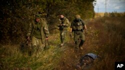 Сили Територіальної оборони України, які розміновують село Гракове на Харківщині, проходять повз тіло загиблого місцевого мешканця, що підірвався на російській міні. 13 жовтня 2022. (AP Photo/Francisco Seco)