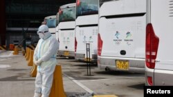 2022北京冬奥会一位身穿防护服的工作人员,他身后是专门接送冬奥会人员的大巴士。