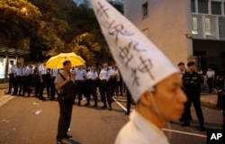 资料照片:在中国文革爆发50周年的第二天,一名抗议者在通往香港政府总部的路上戴着文革时期被批斗者的高帽,反对文革政治,另一位抗议者打着黄雨伞,象征对真普选的诉求。(2016年5月27日)