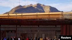 2023年1月5日,移民越过里约布拉沃河后,在美墨边境围栏附近排队申请庇护。(路透社照片)