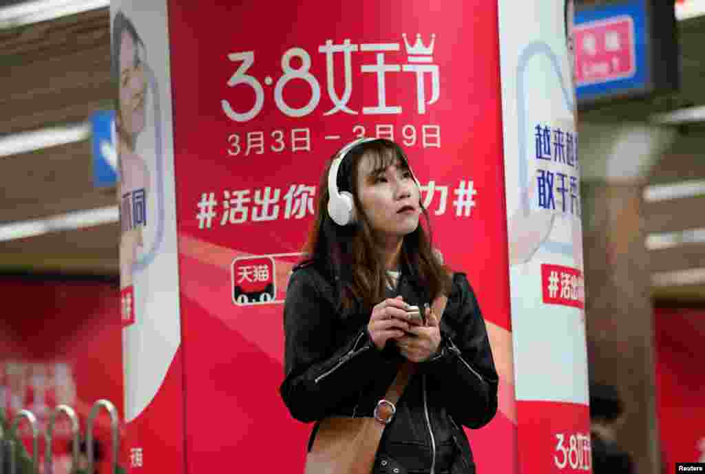 2018年3月7日,北京一个地铁站,一名女子拿着手机,站在阿里巴巴电子商务平台天猫的3·8女王节广告前面。广告说:“活出你的女子力”“越来越多的女人敢于秀美的觉醒”国际妇女节这一天,中国众多商家举行促销行动,将这一天称为“女王节”或“女神节”。有女性权益人士认为,三八节的重点不应是购物,而应关注诸如性骚扰这样严肃的问题。