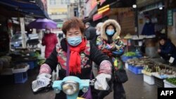 资料照片:一名戴着口罩的妇女骑着电动车穿过武汉市的一个市场。(2020年1月24日)