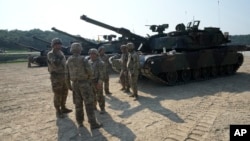 资料照片: 2024年8月14日美国军人站在M1A2艾布拉姆斯坦克旁,准备参加在韩国抱川罗德里格斯实弹演习。