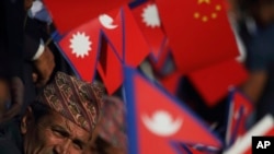 资料照:尼泊尔政府官员手持尼泊尔和中国国旗,在公路旁迎接中国国家主席习近平的到来。(2019年10月12日)