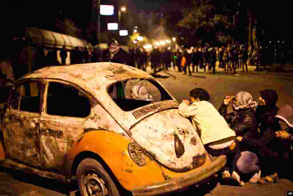 1月28日在埃及的开罗,在与安全部队的冲突中,一名示威者在一辆被损毁的车旁躲避。