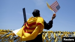 Một người gốc Việt khoát quanh người lá cờ vàng ba sọc đỏ của Việt Nam Cộng Hòa trong khi ông cầu nguyện cạnh 58 ngàn giải băng vàng trên hàng rào đường băng của USS Midway nhân kỷ niệm 40 năm ngày Sài Gòn sụp đổ.