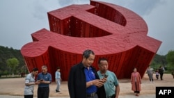 中国民众在延安附近的南泥湾树立的中共镰刀斧子党徽雕塑前拍照。(2021年5月11日)