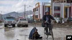 An Afghan man rides his bicycle past a woman and a boy sitting on a flooded street begging for money, following a heavy rain in Kabul, Afghanistan, April 2, 2014.