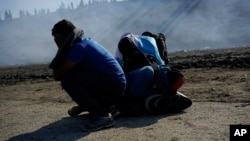 在美国巡逻队员对美墨边境发射催泪瓦斯的情况下,三名洪都拉斯移民挤在河岸边。 他们和一群移民在2018年11月25日在墨西哥蒂华纳过境后越过墨西哥警方。