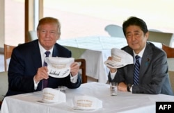 在东京附近的高尔夫球场俱乐部共进午餐时,唐纳德·川普和安倍晋三在白色球帽上签名,帽子上印着“唐纳德和晋三使同盟更伟大”(2017年11月5日)
