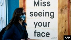 2020年4月1日新冠病毒爆发期间,一名戴着口罩的女士走过封闭的餐馆: 门上写着:想念你们。