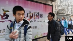 2018年3月12日,北京一所学校外面,青少年走过宣传牌,牌上写着中英文口号“点亮中国梦 知识改变命运 付出收获财富”。