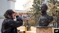 A woman prays at a bust of the last Russian Czar Nicholas II placed near the Crimean prosecutor's office, foreground, in Simferopol, Crimea, March 6, 2017.