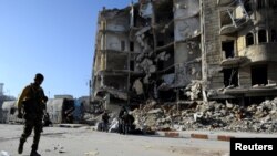 A member of Forces loyal to Syria's President Bashar al-Assad carries his weapon as he walks past damaged buildings in a government held area of Aleppo, Syria Dec. 9, 2016.
