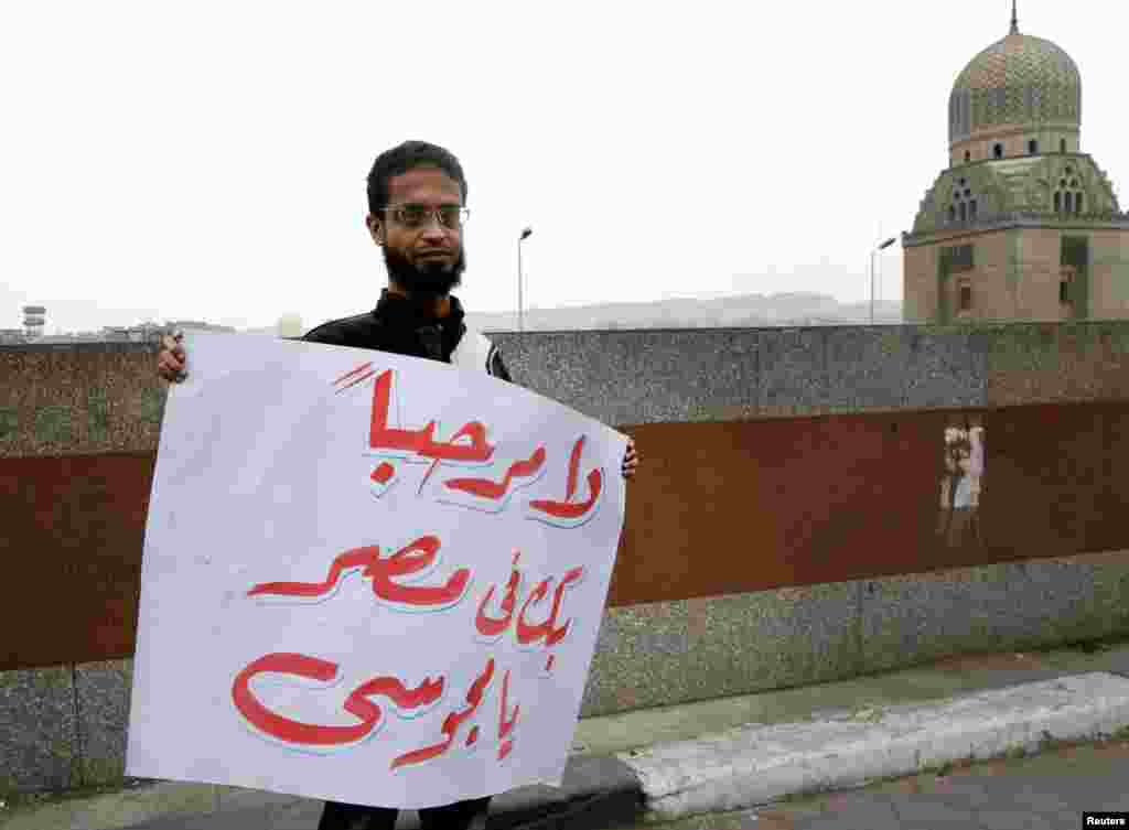 当伊朗总统艾哈迈迪内贾德2013年2月5日访问开罗时,一个人在爱资本哈尔清真寺前面举着用阿拉伯文书写的“(艾哈迈迪内贾德)你在埃及不受欢迎”的牌子。