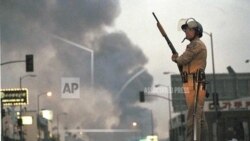 一名加州公路巡警在洛杉矶第九街和佛蒙特州大道站岗,大火中升起浓烟。这是洛杉矶骚乱的第二天,此前罗德尼·金(Rodney King)殴打案中的四名洛杉矶警察被无罪释放。(1992年4月30日)(美联社图片 )