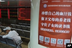 北京一名投资者坐在一个股票交易所内树立的一张海报旁。海报上写道:“珍惜自己的血汗钱,保卫父母的养老钱,守住子女的读书钱“。(2019年6月12日)