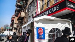 布鲁克林一家急诊室的帐篷,招牌上告诉怀疑自己感染冠状病毒的人到里面等候检测。(美联社)