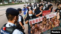 香港支持民主的四名抗议者在中国国庆这一天不惧警察的监视,手举标语牌要求释放政治犯。(2021年10月1日)