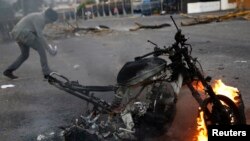Một người biểu tình chống chính phủ đi qua một chiếc xe máy bị đốt sau một cuộc biểu tình ở San Cristobal,Venezuela, 27/2/2014.