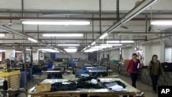 中国广东省中山市南朗镇翠亨制包厂工人罢工,几名工人走过车间里处于停工状态的工作台,2015年3月26日(资料图)