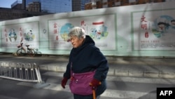 一名中国妇女走过北京一处建筑工地,背后的宣传牌上写着“文明”“民主”“富强”“友善”“诚信”。(法新社 2018年12月4日)