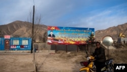 2018年3月2日,青海铜仁高速公路旁,一名骑摩托车的人驶过宣传牌,牌上有中国国家主席习近平像和中文藏文标语“人民对美好生活的向往,就是我们的奋斗目标”。