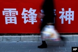 北京街头,一位女士路过宣传雷锋精神的广告标语(2019年3月5日)