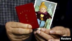 资料照:中国张家口市一家玻璃厂60岁的老工人江卫矛(音)和53岁的妻子手拿他们死亡的独生子在孩童时期的照片和独生子女证。(2015年11月21日)