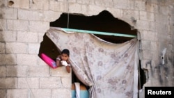 Một cậu bé Palestine ngồi nhìn ra ngoài từ ngôi nhà bị hư hại vì đạn pháo của Israel.
