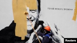 资料照:俄罗斯圣彼得堡的一个工人在涂抹掉俄罗斯反对派领导人阿列克谢·纳瓦尔尼(Aleksey Navalny)的画像,画像旁写着“新时代的英雄”。(2021年4月28日)