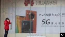 疫情期间一名妇女站在位于北京的华为手机5G广告旁。(2020年3月8日)