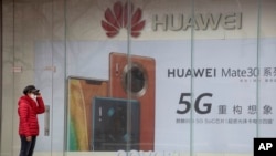 北京,一位戴着口罩的妇女站在华为手机广告旁(2020年3月8日)。