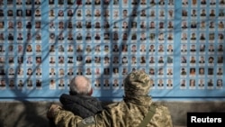 资料照:两名身穿迷彩服的男子在乌克兰基辅纪念墙前向在俄乌战争中牺牲的士兵致敬。(2023年3月14日)