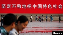 资料照:人们走过北京天安门广场竖立的一幅宣传中国特色社会主义道路的巨幅标语。(2012年6月3日)