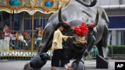 资料照:一名妇女在北京一家零售和批发服装商场外面铜牛雕塑旁边。(2018年7月9日)