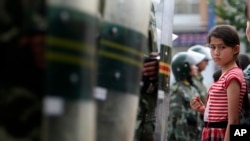 2009年7.5事件后,乌鲁木齐的一名维吾尔族女孩注视着一排中国防暴警察。(2009年7月9日)