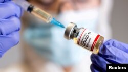FILE PHOTO: A woman holds a small bottle labelled with a "Coronavirus COVID-19 Vaccine" sticker and a medical syringe in this illustration taken October 30, 2020.
